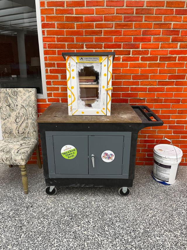 A trolley with a wooden box with a glass front on reading &lsquo;Little Free Library&rsquo;