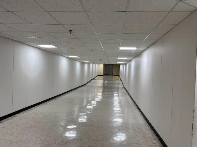A completely empty, white corridor with fluorescent lighting and gray floor tiles