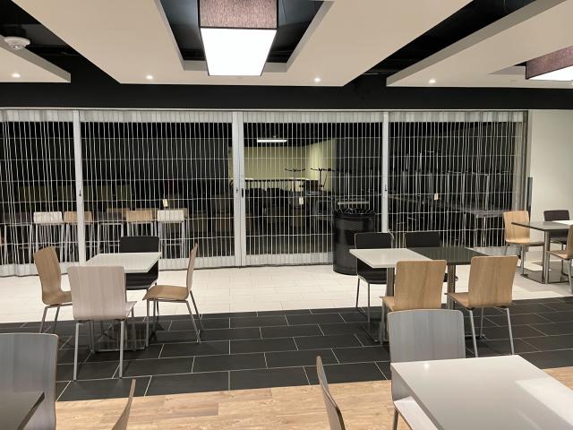 Fluorescent lit tables and chairs with a shuttered food outlet in the background in darkness.