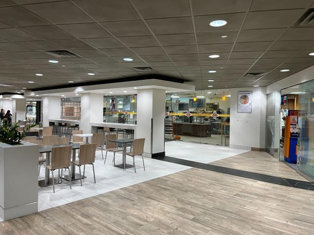 Fluorescent lit tables and chairs with with a real food outlet behind, with a off-license type shop to the right.