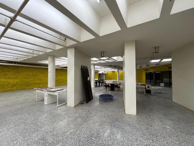 A yellow walled room with fluorescent lights, tables and chairs and a trampoline