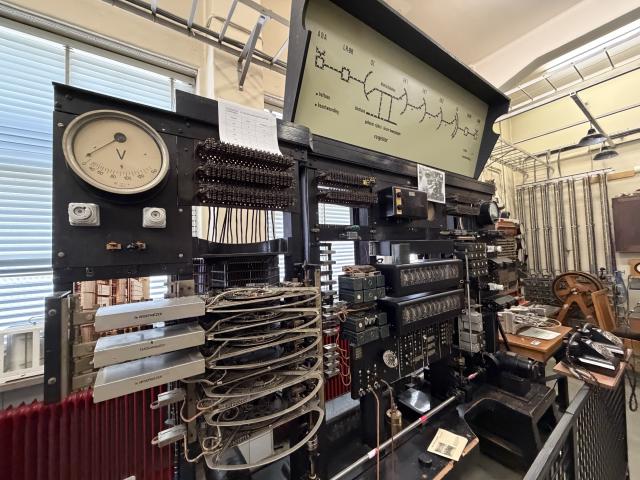 A large black machine with lots of dials and old telephones and switches and relays with a light up diagram at the top