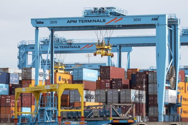 Four large blue cranes with APM TERMINALS written on them with hundreds of different color shipping containers underneath them