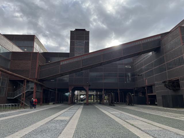 A large building that looks to be made of brick with rails going underneath embedded in the ground with a diagonal part in front.
